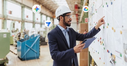 A man wearing a white hard hat looks at a table and physical board of projects