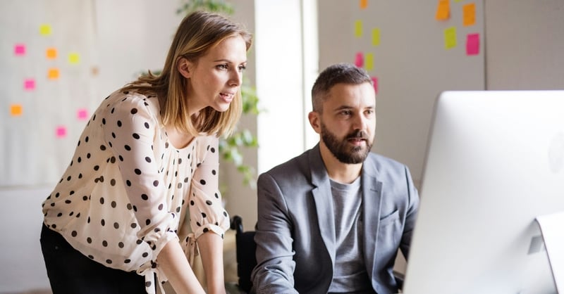 Two colleagues review information on a desktop computer in a modern office setting 
