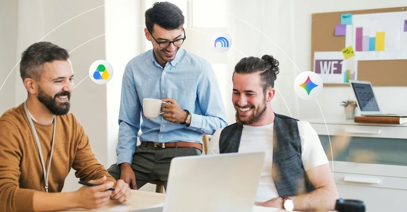 Three men sitting in a modern office setting looking at the same laptop screen