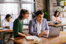 A young woman looks over her coworker's shoulder at this Chromebook screen