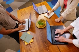 A group of office workers sit around a table on their Chromebooks