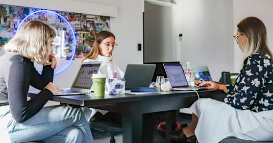 A photograph featuring three stylish young professionals working from their laptops in a modern office setting