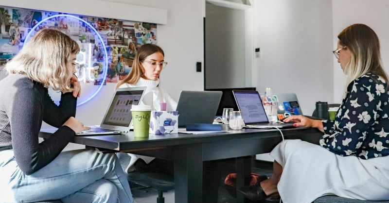 A photograph featuring three stylish young professionals working from their laptops in a modern office setting
