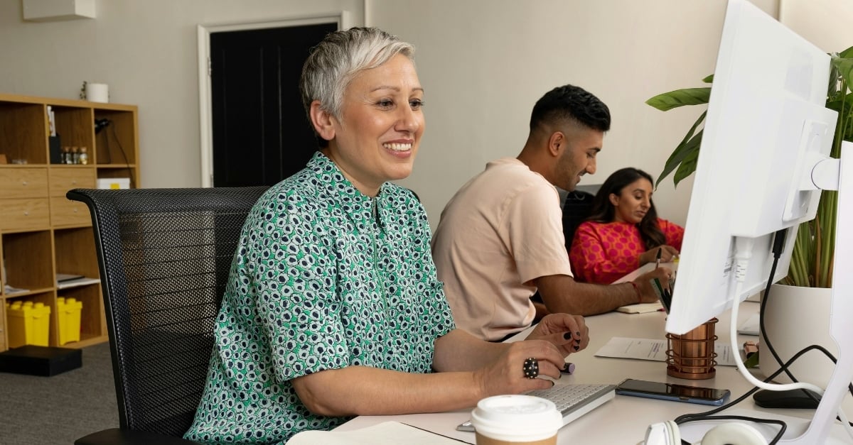 A woman smiles at her desktop monitor while sitting in a modern, professional office 