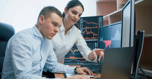Two professionals look at data together on a desktop monitor