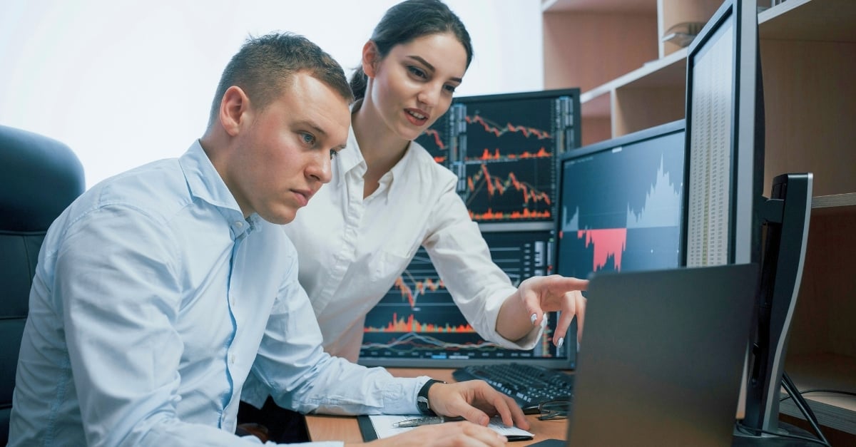 Two professionals look at data together on a desktop monitor