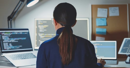 A professional office worker reviews code on various screens in a modern setting 