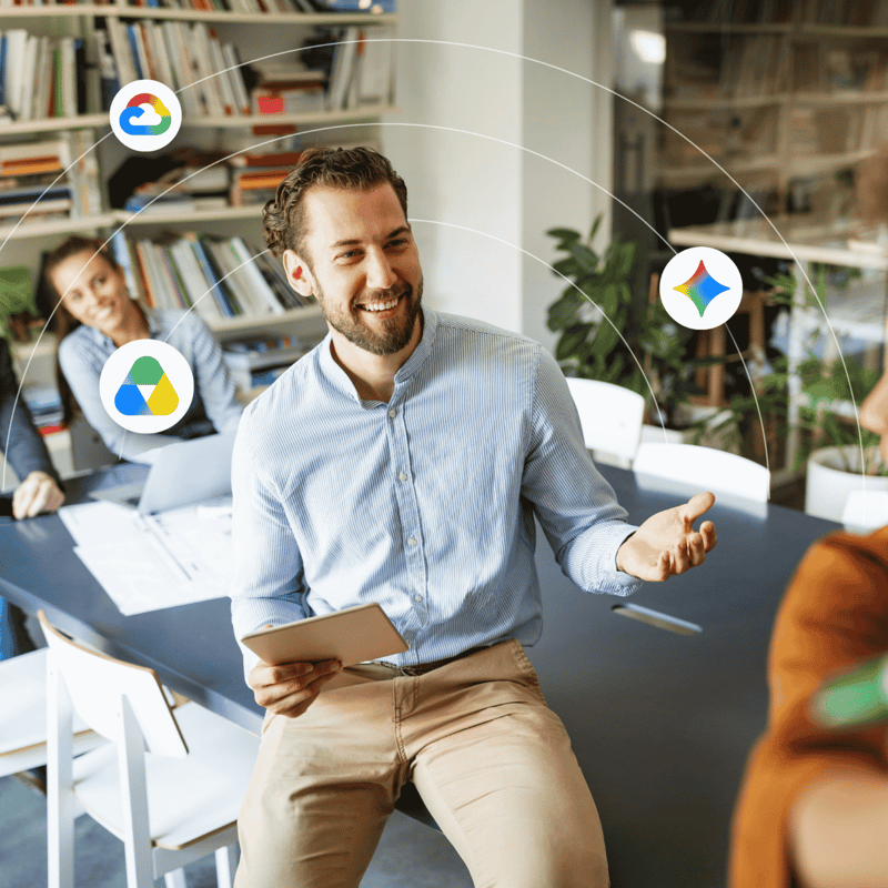 A man sits on the edge of a table while talking to his coworkers