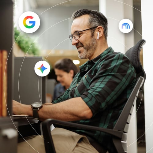 A professional man sits at his desk surrounded by floating Google product icons